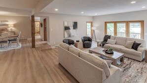 A spacious living room with a large sofa, a coffee table, and a dining area with a table and chairs. - Gorgeous Waterfront Retreat (Pequot Lakes)
