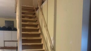 Eine Holztreppe führt zu einer oberen Etage, an einer Seite befindet sich ein Geländer.