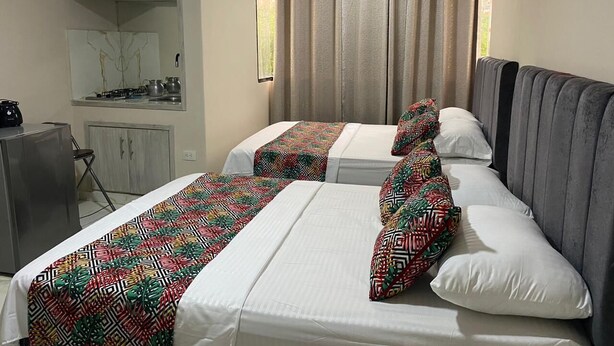A hotel room with two beds, a kitchenette, and a window with curtains. - Beach Apartments Nabusimake (Santa Marta)