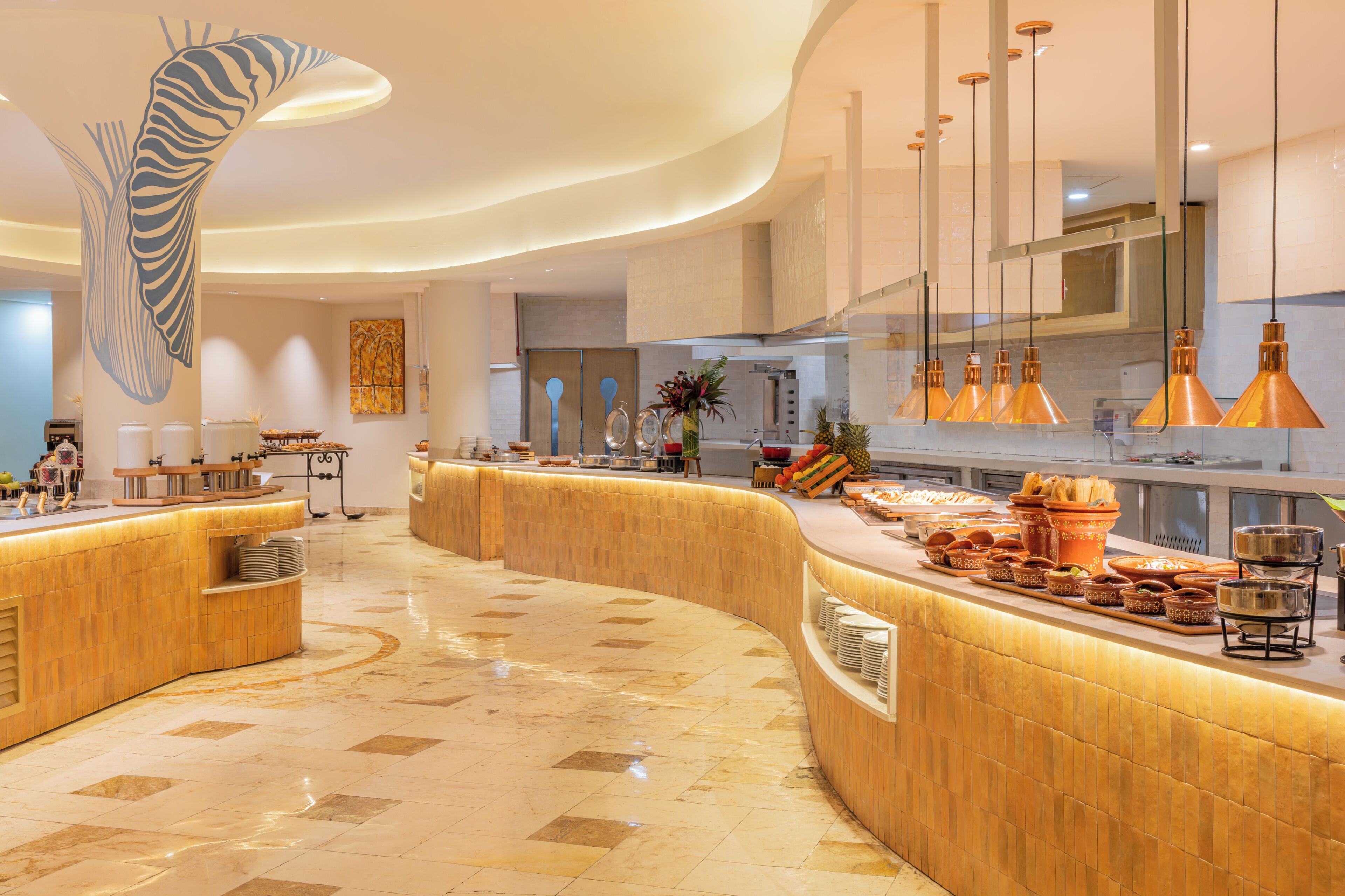 A modern hotel lobby with a curved reception desk, a large abstract wall art piece, and a buffet area with various food items.