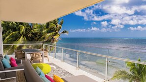 Een balkon met uitzicht op de oceaan, voorzien van een bank en stoelen, en een tropische muurschildering.