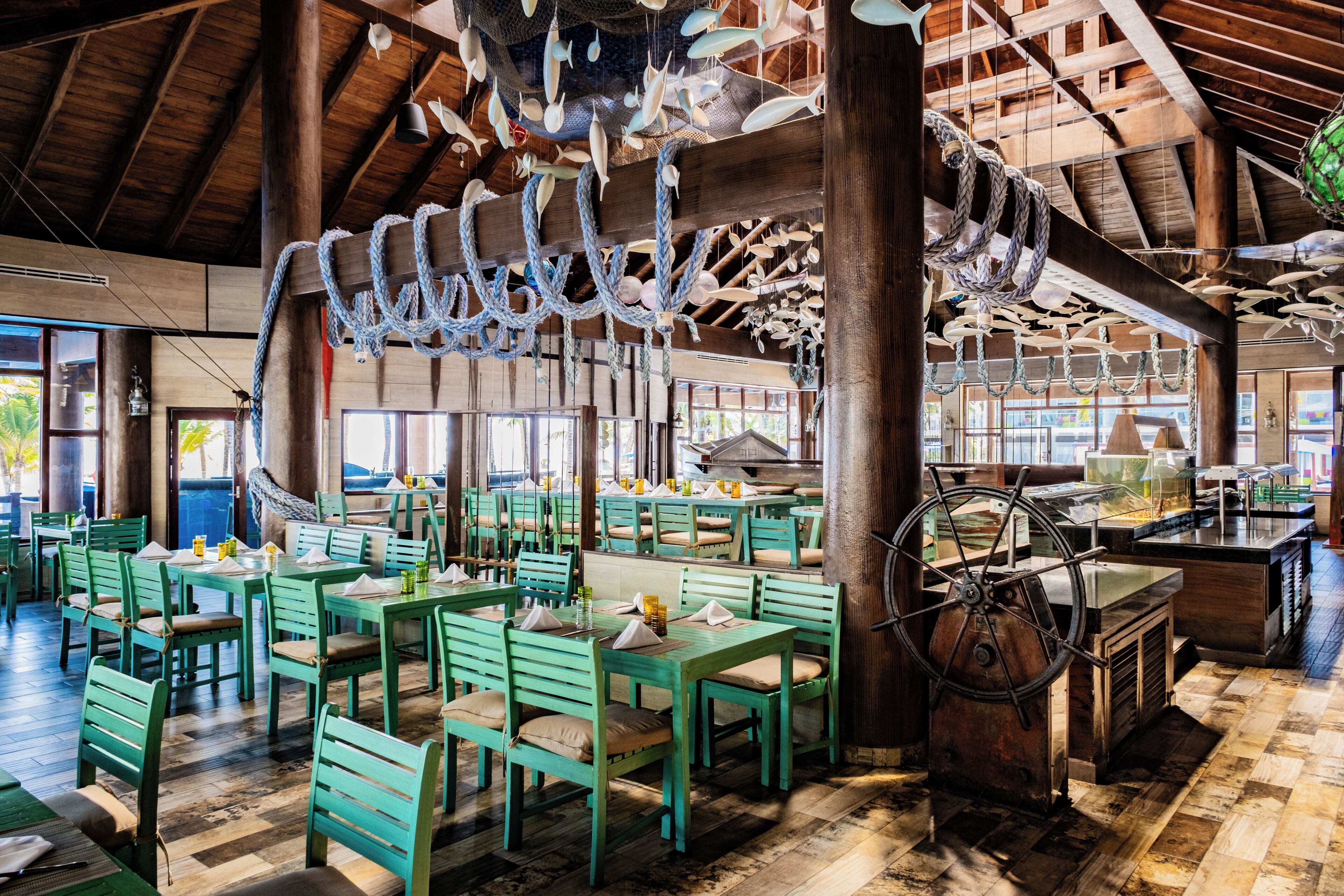 A restaurant with wooden beams, green chairs, and tables.