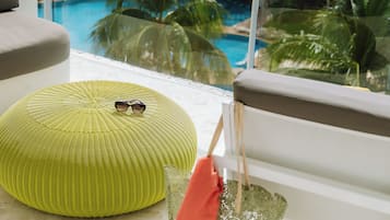 A balcony with a view of a swimming pool, palm trees, and a thatched-roof building.