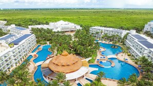 Een resort met meerdere zwembaden, palmbomen en een groot gebouw met een rieten dak.