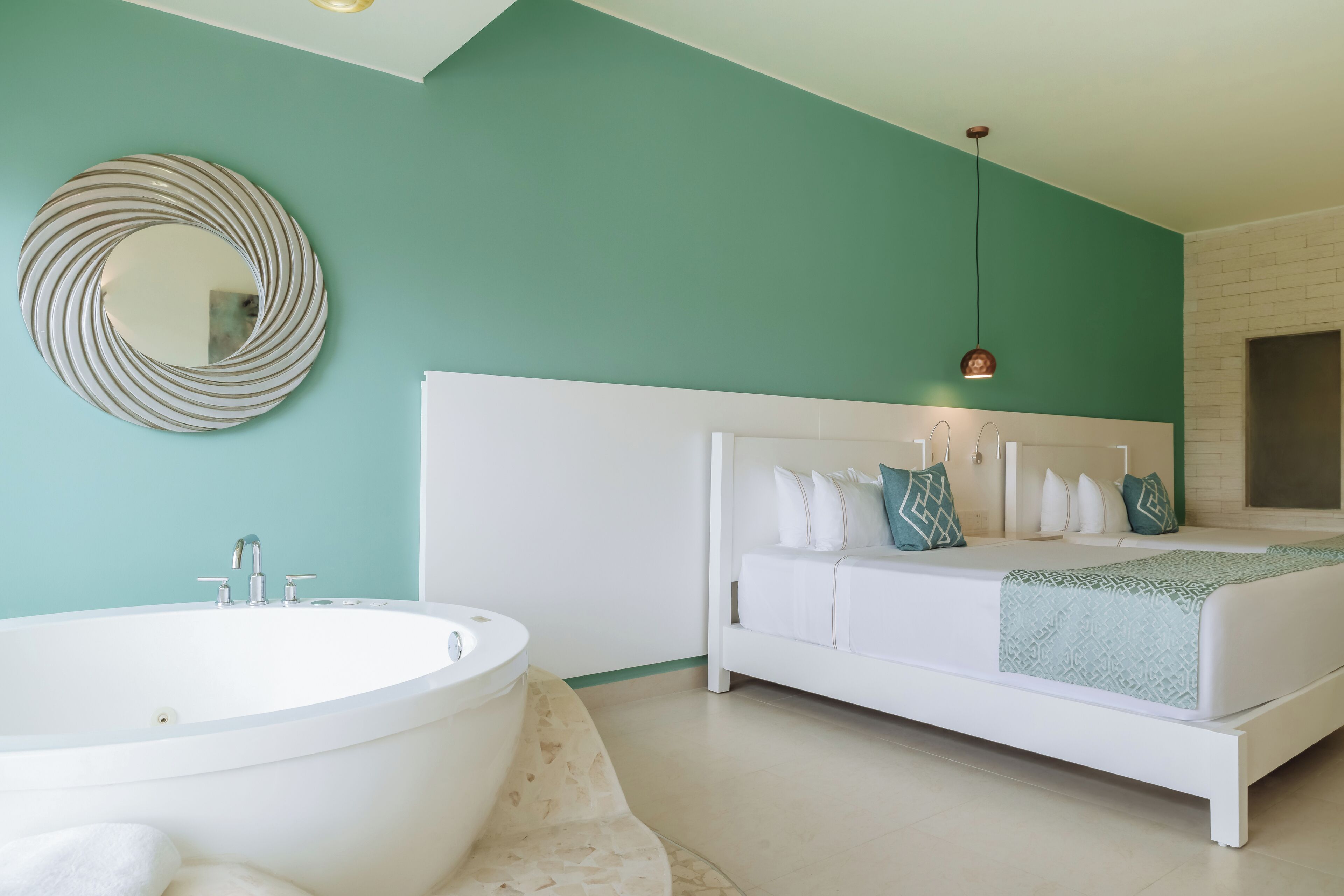 A modern bedroom with a large white bathtub, a white bed with patterned pillows, and a green accent wall.
