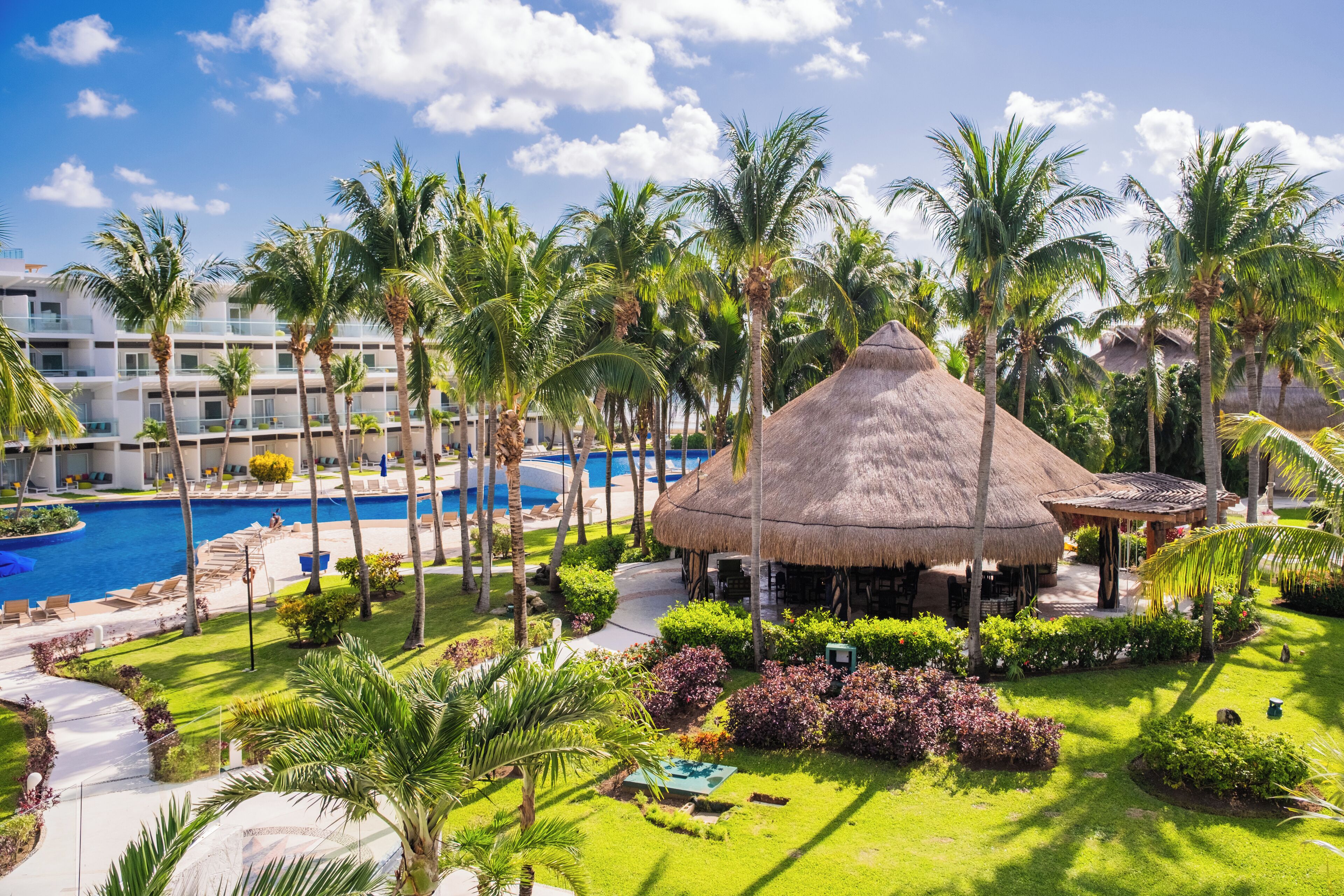 A resort with a pool, palm trees, and a thatched-roof structure.