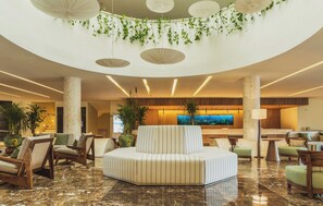 A spacious lobby with a central seating area, multiple plants, and a large screen. - Iberostar Selection Riviera Cancún - All Inclusive (Puerto Morelos)