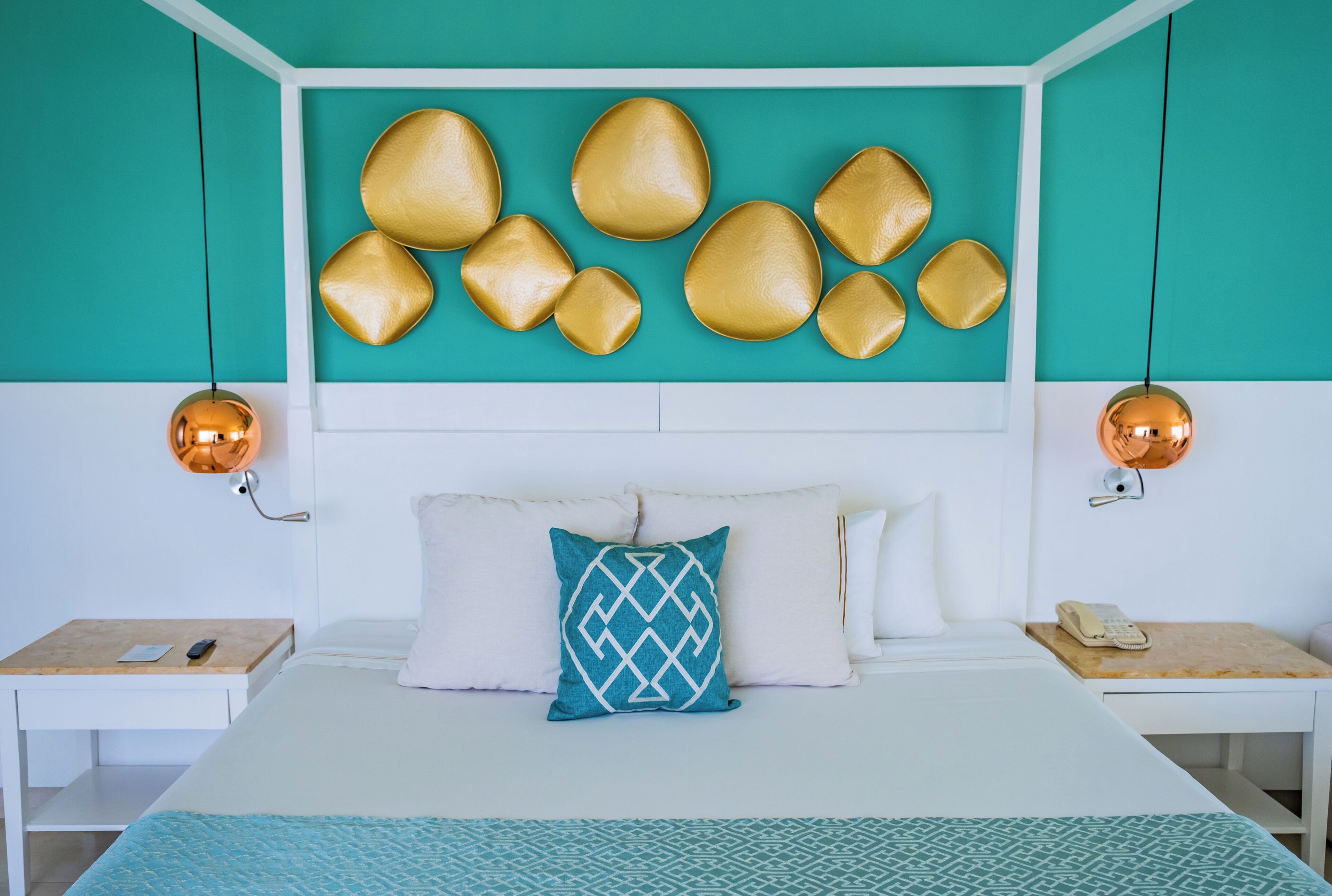 Une chambre d’hôtel moderne avec un mur d’accent de couleur turquoise, une tête de lit blanche et une couvre-lit à motifs.