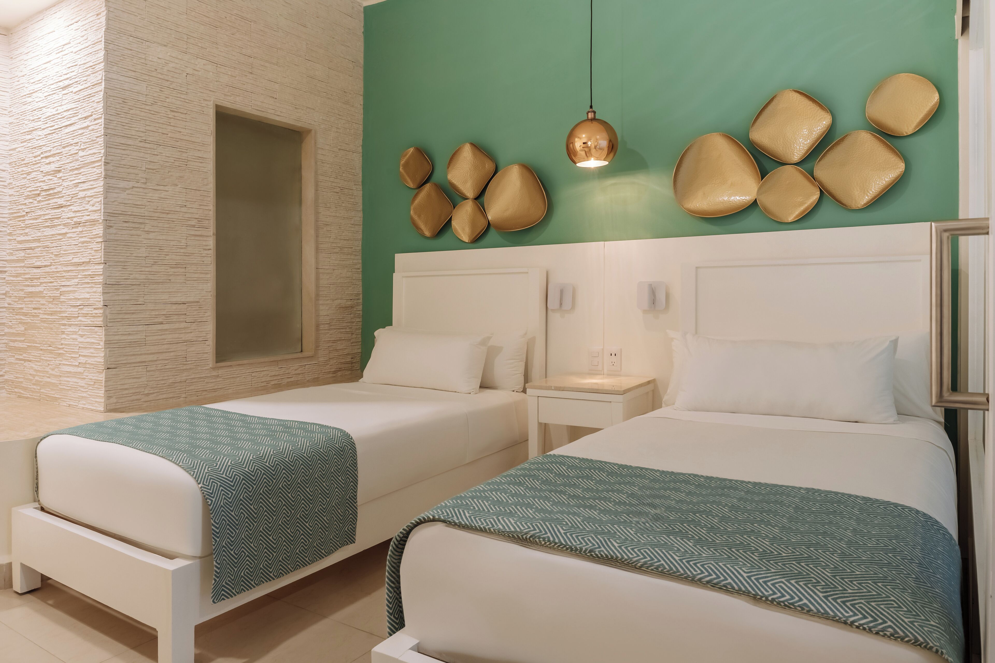 A hotel room with two beds, a large window, a wall-mounted light fixture, and a textured wall.