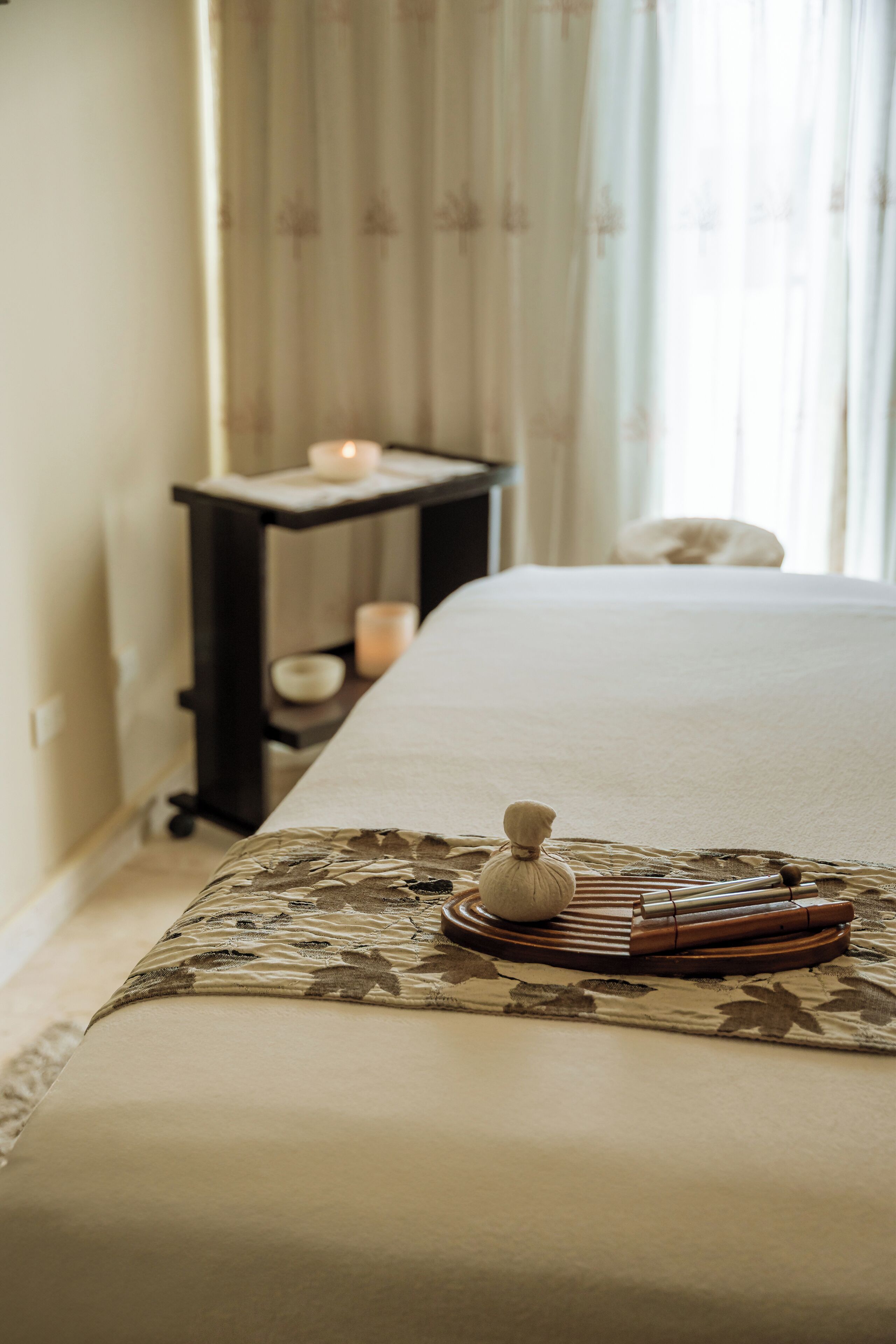A neatly made bed with a floral-patterned bedspread, a wooden footrest, and a small decorative item on the bed.