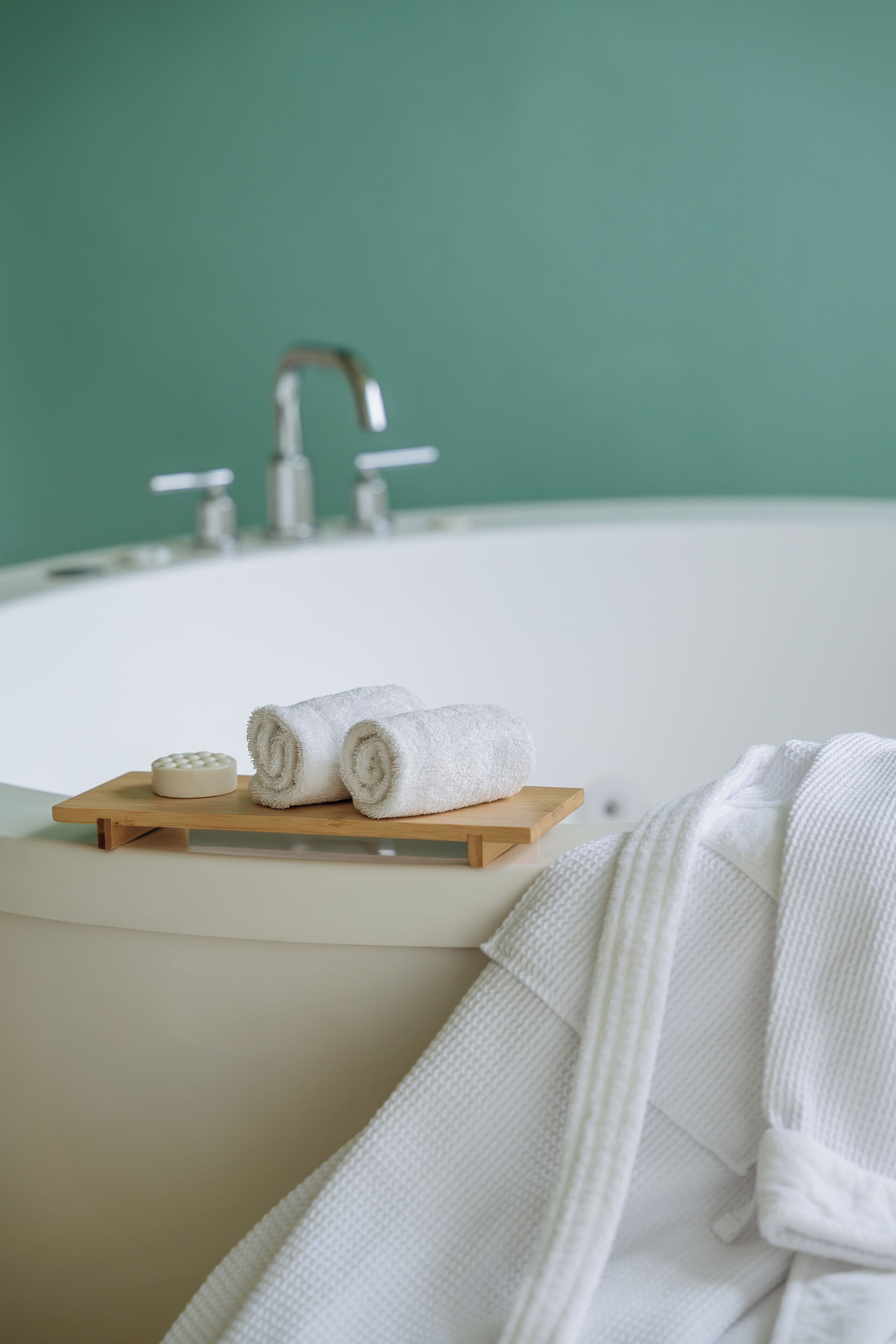 Un baño con una bañera, una bandeja de madera con una pastilla de jabón y dos toallas enrolladas, y una bata de baño blanca colgada sobre la bañera.