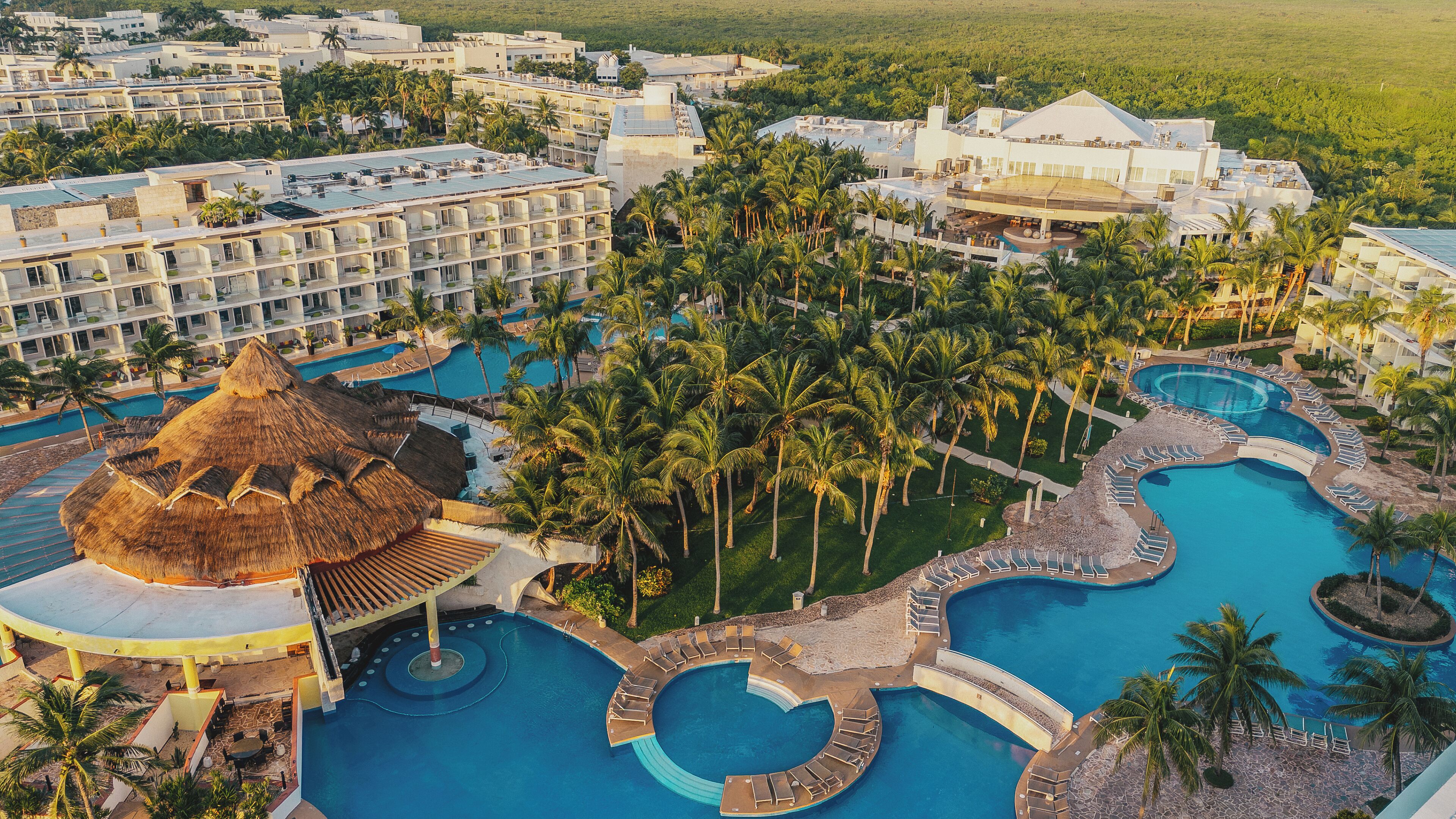A resort with multiple swimming pools, palm trees, and a large building with a thatched roof.