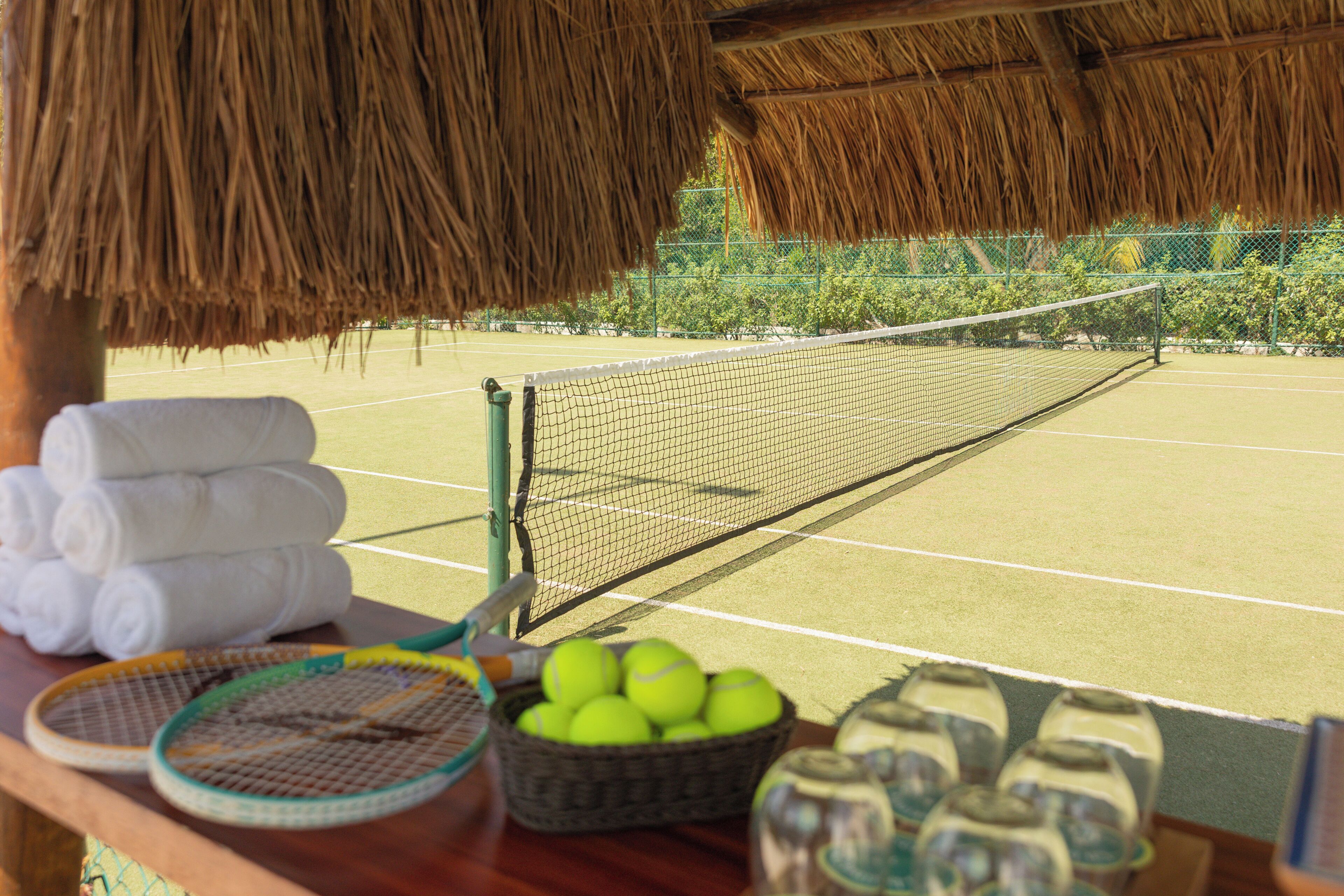 A tennis court with a net, a basket of tennis balls, and a rack of towels.