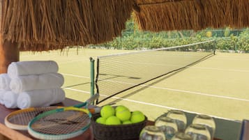 Una cancha de tenis con una red, una cesta de pelotas de tenis y un escurridor de toallas.