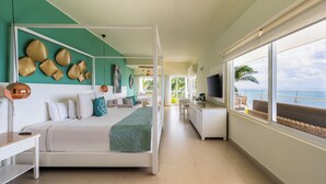 Een moderne hotelkamer met een bed, een bureau, een televisie en een balkon met uitzicht op de oceaan.