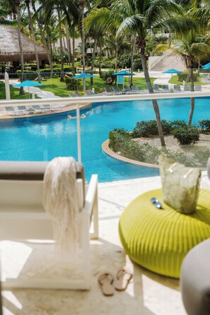 A pool area with lounge chairs and umbrellas, surrounded by palm trees and a thatched-roof building. - Iberostar Selection Riviera Cancún - All Inclusive (Puerto Morelos)