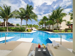 A pool area with lounge chairs, a drink on the table, and palm trees. - Iberostar Selection Riviera Cancún - All Inclusive (Puerto Morelos)