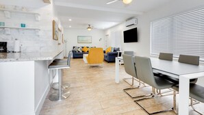A modern kitchen with white marble countertops, a dining area with a white table and grey chairs, and a living area with a sofa and yellow armchair. - Spacious 1 Bedroom Apartment, Steps from the beach (Hollywood)