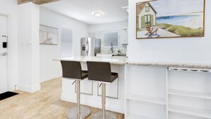 A modern kitchen with white cabinets, a stainless steel refrigerator, and a bar area with two stools. - Spacious 1 Bedroom Apartment, Steps from the beach (Hollywood)