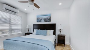 A bedroom with a bed, two bedside tables with lamps, a ceiling fan, an air conditioning unit, and a picture on the wall. - Spacious 1 Bedroom Apartment, Steps from the beach (Hollywood)