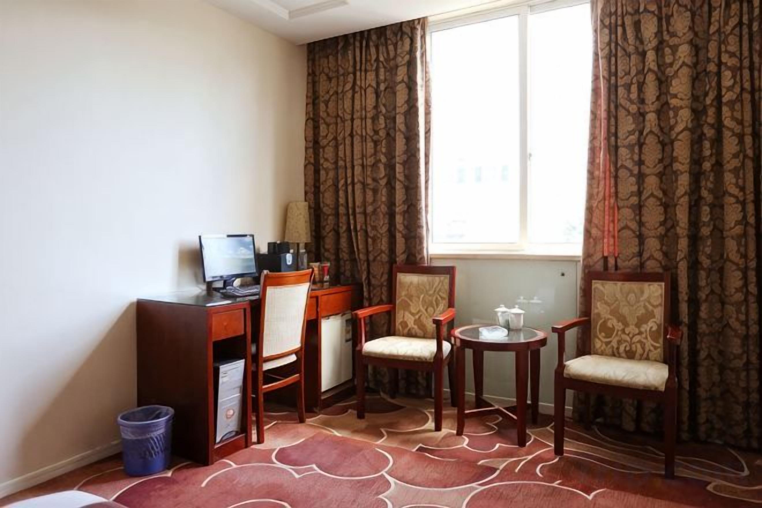 Una habitación de hotel con escritorio, dos sillas, una mesita y una ventana.