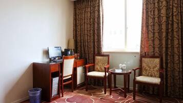 Una habitación de hotel con escritorio, dos sillas, una mesita y una ventana.