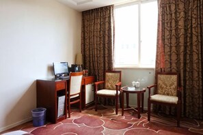 Une chambre d’hôtel équipée d’un bureau, de deux chaises, d’une petite table et d’une fenêtre.
