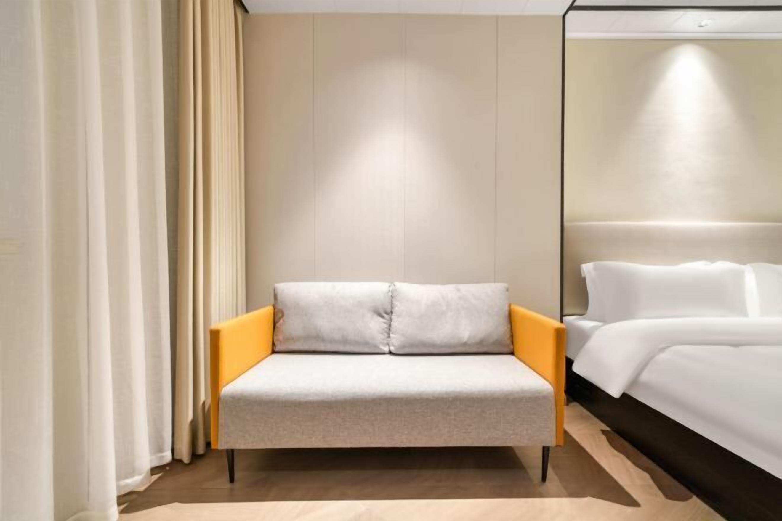 Une chambre d’hôtel moderne dotée d’un canapé-lit, d’un lit séparé et d’une grande fenêtre avec des rideaux.
