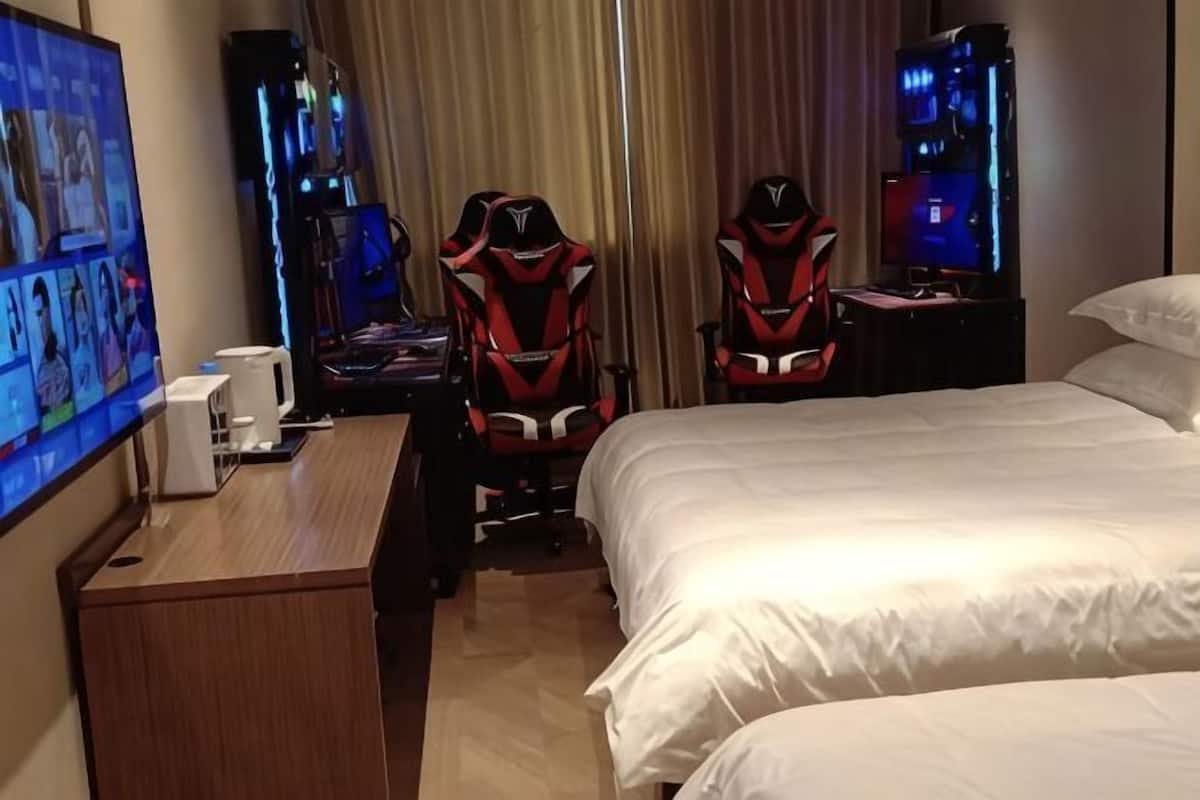 A hotel room with a bed, two gaming chairs, a desk with a computer, and a TV.