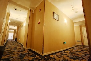 Un couloir d’hôtel avec un sol recouvert de moquette, une porte sur la droite et un interrupteur sur le mur.