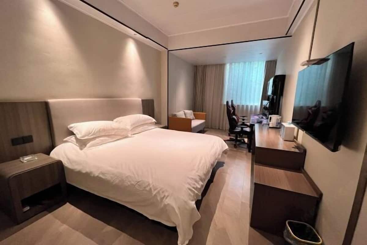 A modern hotel room with a large bed, a desk, a chair, a TV, and a mirror.