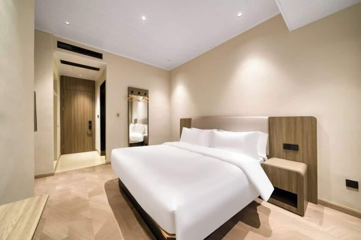 A modern hotel room with a large bed, wooden headboard, and a walk-in closet.