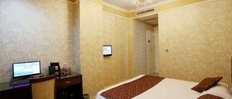 A hotel room with a bed, a desk with a computer, and a television.