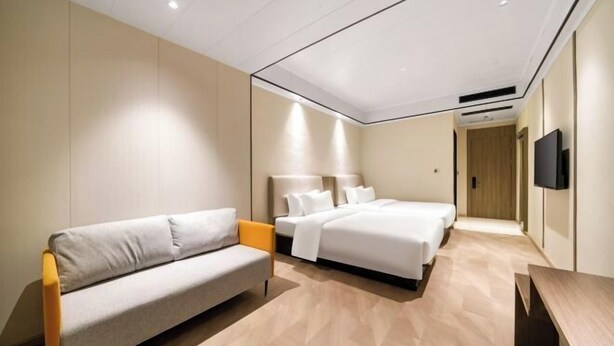 Una moderna camera d'albergo con divano, due letti, una TV a schermo piatto e pavimento in legno.