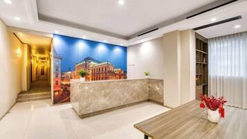 A hotel lobby with a reception desk, a large mural, a staircase, and a dining area.