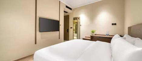 Habitación de hotel con cama, televisor montado en la pared, un pequeño escritorio con una planta y un espejo.