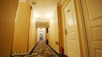 A hotel hallway with carpeted flooring, white doors, and a fire extinguisher on the wall.