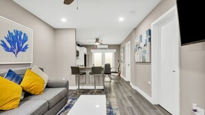 Un salon moderne avec un canapé gris, des coussins jaunes, une table basse blanche et un tapis à motifs bleus et blancs.