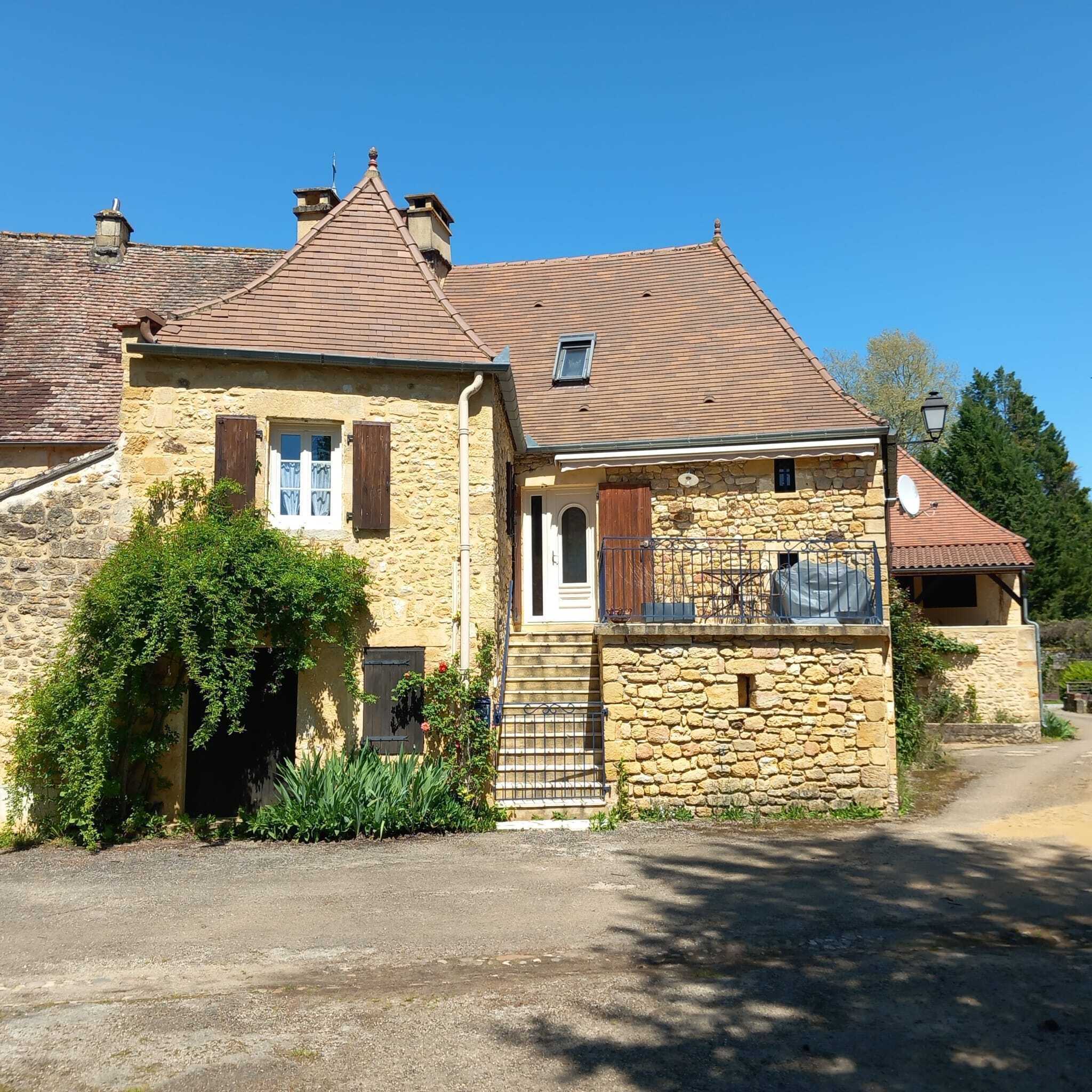 Une maison en pierre avec un toit en tuiles, un petit balcon et une allée gravillonnée.