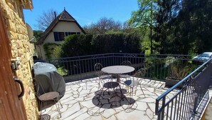 A patio with a stone floor, a round table, and chairs. There is a metal fence and a house in the background.