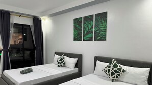 Een hotelkamer met twee eenpersoonsbedden, een groot raam met gordijnen, en een muur met drie kunstwerken met bladmotieven.