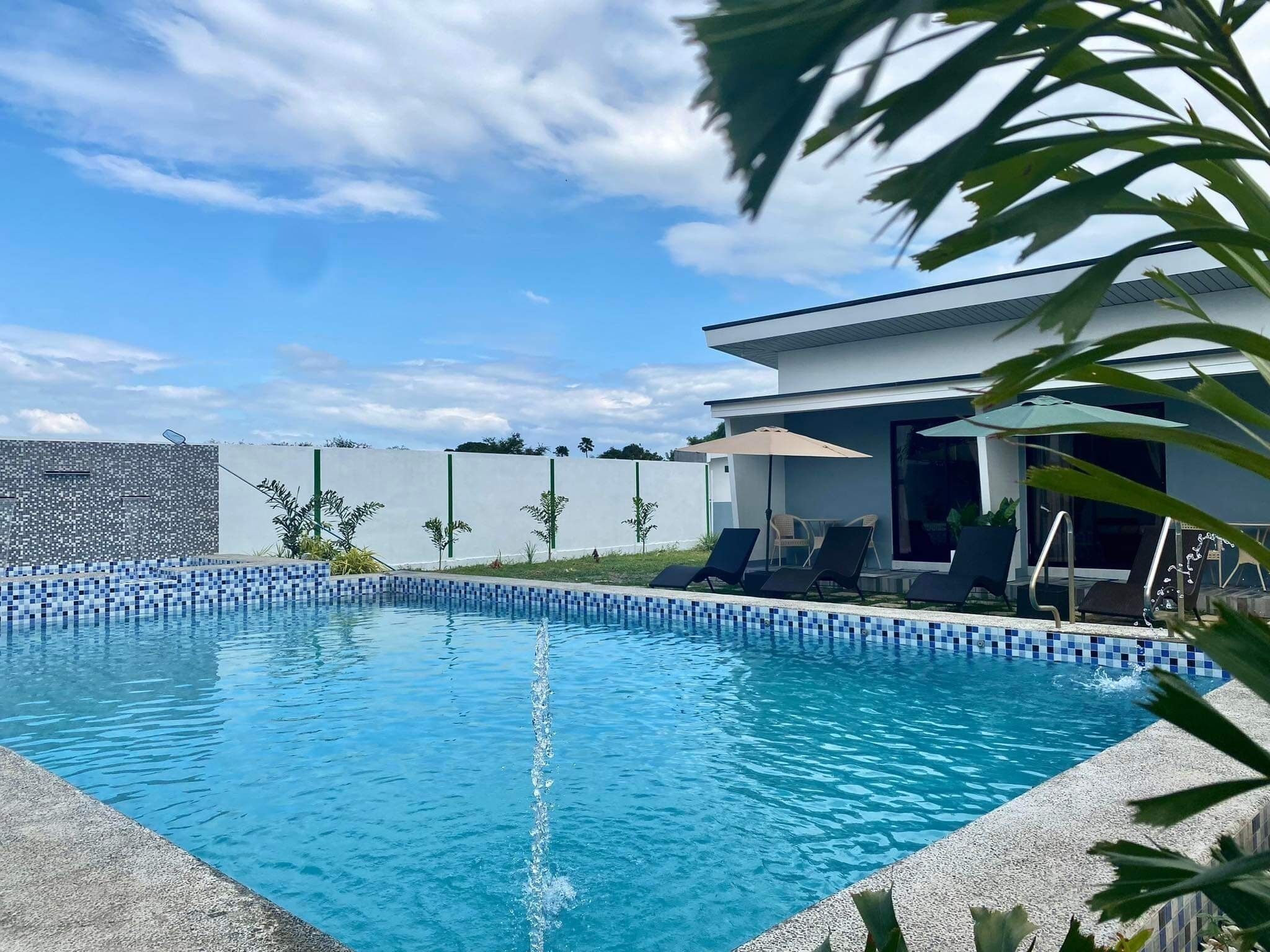 A modern pool area with a clear blue pool, lounge chairs, and a white building with large windows.