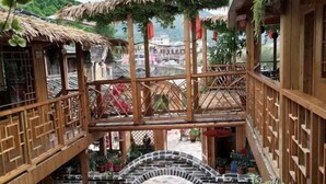 A multi-level wooden structure with a thatched roof, a stone archway, and potted plants. - Waiting For You at Yunshuiyao Inn (Nanjing County)