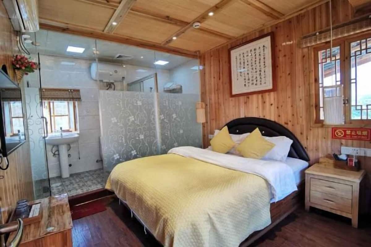 A wooden-paneled room with a bed, a bedside table, a mirror, a sink, and a shower area.
