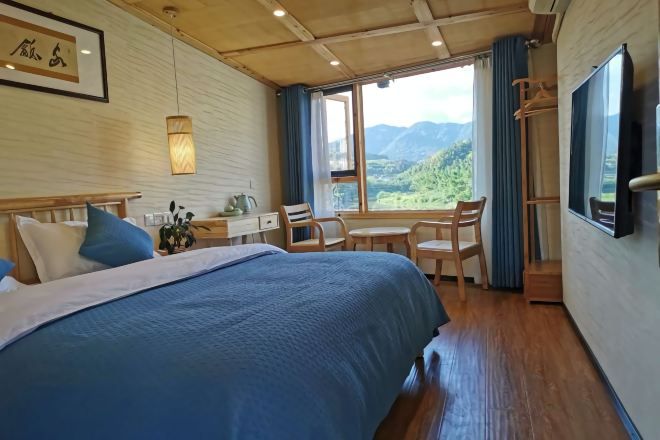 Un dormitorio con una cama grande, un escritorio y una silla. Hay una ventana con vistas a montañas.