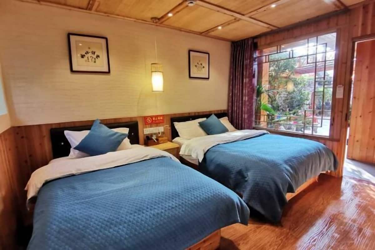 A room with two beds, wooden walls, and a window with a view of greenery.