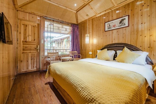 Una habitación de madera con una cama, un televisor, una ventana con cortinas y un cuadro en la pared.