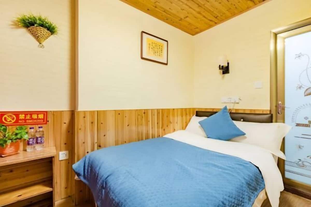 A room with a bed, a wooden headboard, a wall-mounted light, a framed picture, and a no-smoking sign.