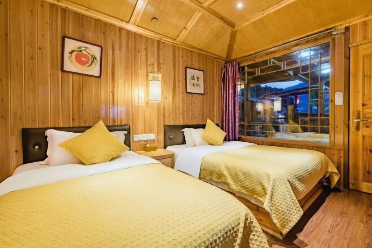 A wooden room with two beds, a window with curtains, and a wall-mounted light fixture.
