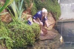 Una estatua de una persona agachada junto a un estanque, sosteniendo una caña de pescar.